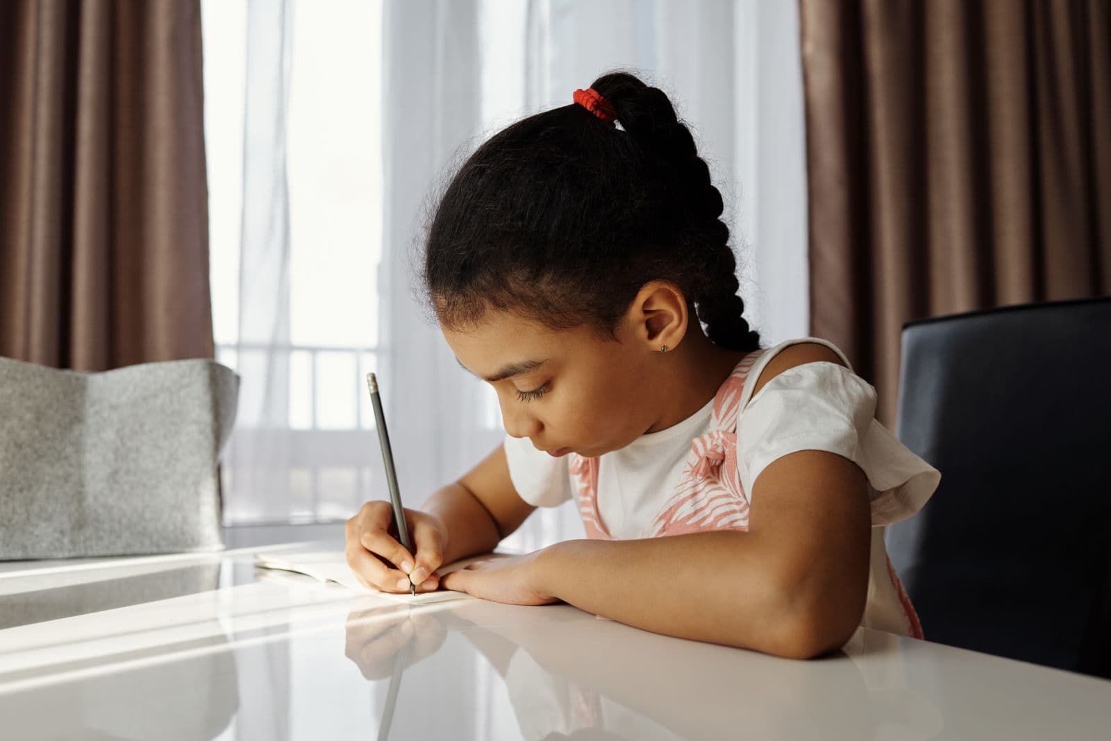 A focused primary-school girl writing at a desk in calm, natural light.