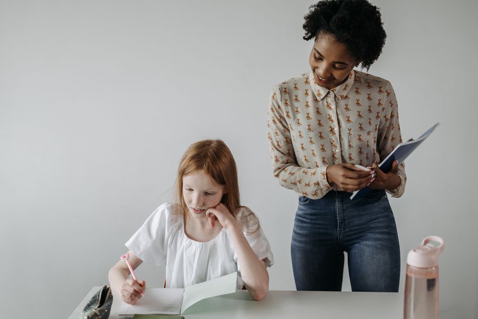 An educator sitting beside a primary-school child, working through a page at the child’s own level.