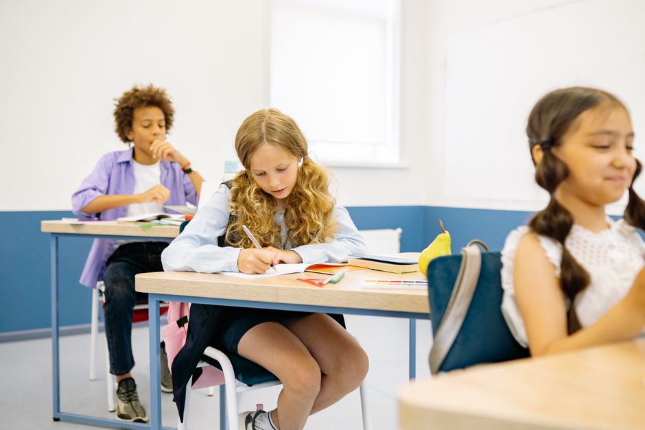 A classroom of primary-school children at their desks, all working on the same page at the same time.