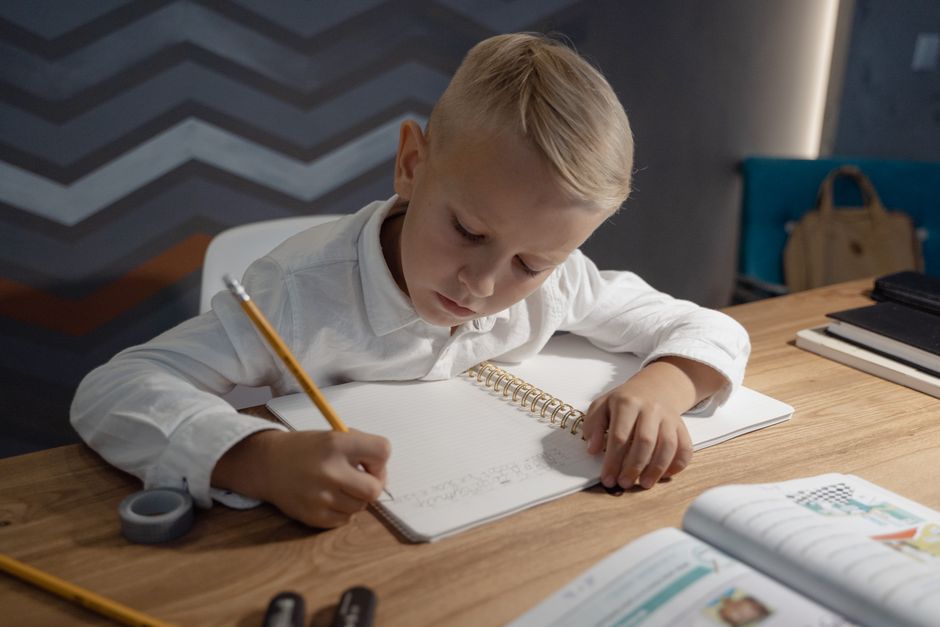 A primary-school child studying calmly at a tidy desk with notes and a practice paper, looking focused rather than stressed.