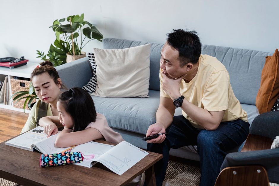 A parent sitting calmly beside their child at the kitchen table, listening as the child explains a topic from their notes.