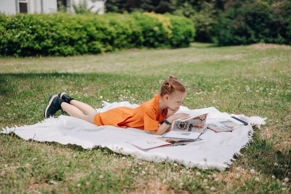 A child reading a library book on a picnic rug in a Melbourne park on a sunny holiday afternoon.