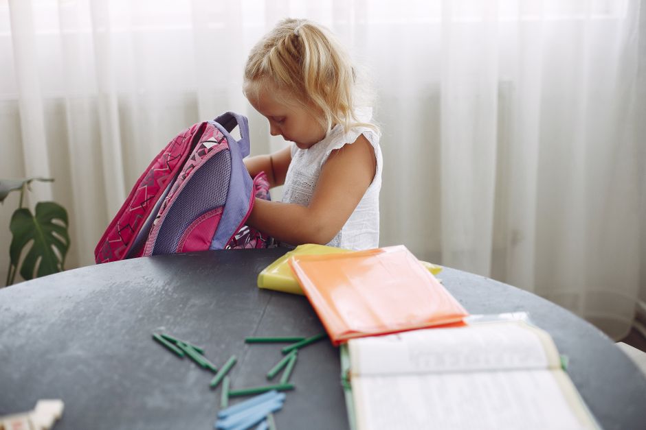 A primary-school child in uniform packing a school bag at the kitchen table on the first morning back.