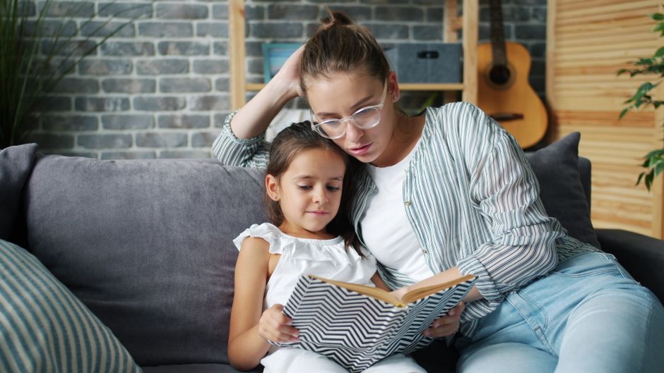 A parent and child sharing a book together on the sofa, both smiling as they read.